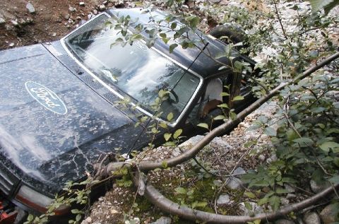 1993 Ford Bronco - A black Ford Bronco is seen partially buried in a ditch, surrounded by rocks and branches.