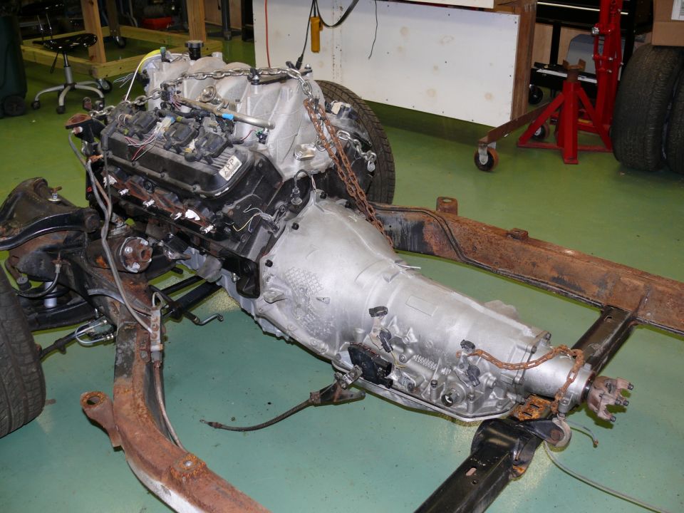 Engine and transmission assembly suspended by chains, resting on a frame