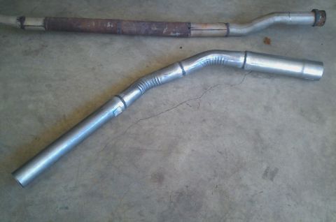 1987 Ford Bronco - Two exhaust pipes, one old and rusted, the other new and shiny, lie on a concrete surface.