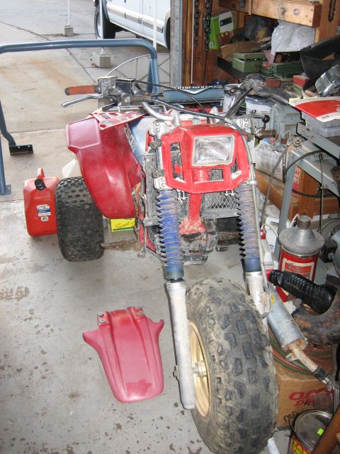 1900 Honda Big Red - This three-wheeled ATV is in a garage with tools and supplies in the background.