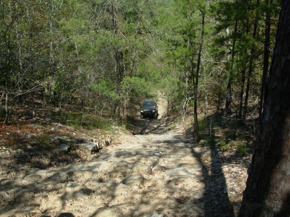 Dark SUV descending a rocky forest trail in the distance