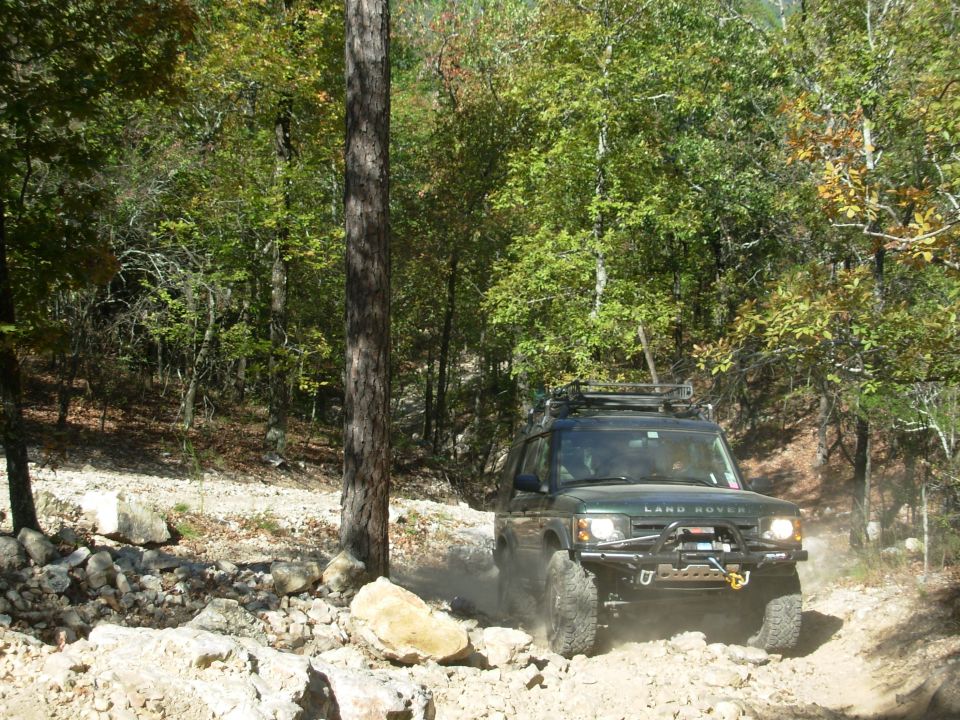 Green Land Rover Discovery with headlights on a rocky forest trail