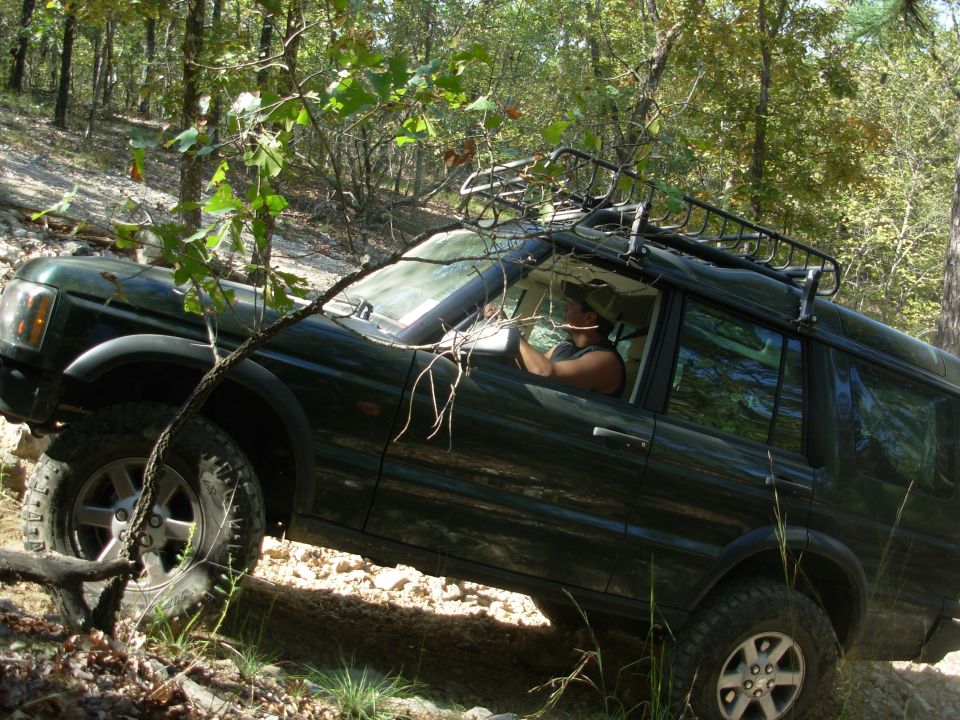 Green Land Rover Discovery tilted on an off-road obstacle in the woods