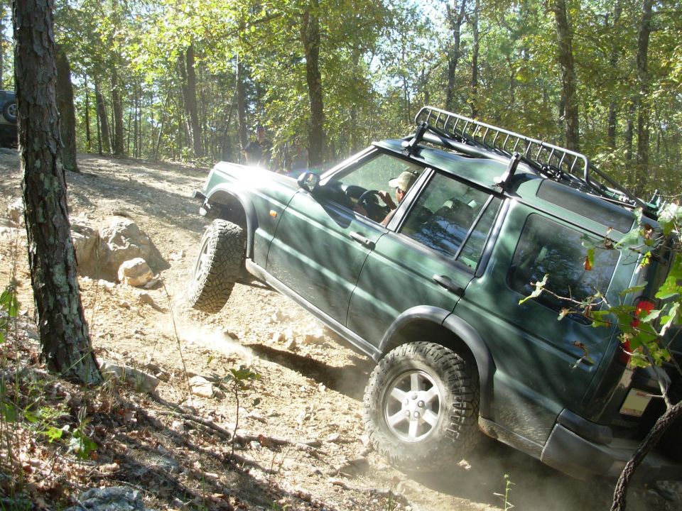 Green Land Rover Discovery flexing over rocks on a forest trail
