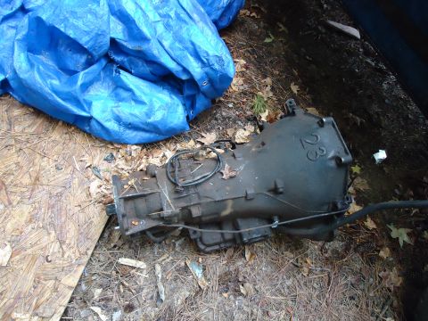 1985 Ford Bronco - Transmission part with cast numbers visible, outdoors next to a blue tarp.