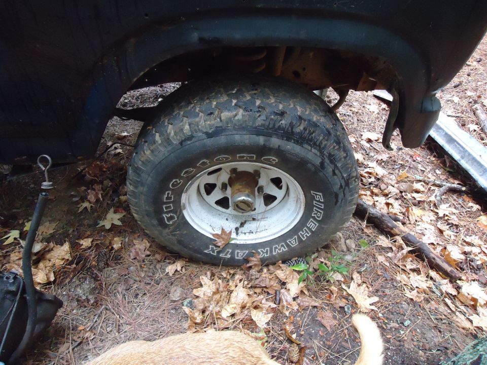 Close-up of a vehicle's front tire and fender, with the wheel showing Firehawk ATX branding. Some debris and leaves are on the ground