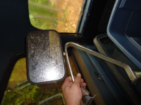 1985 Ford Bronco - Interior view of a vehicle's side mirror and door trim, with a hand adjusting the mirror.