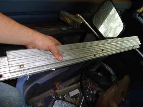 1985 Ford Bronco - An aluminum trim piece is held by a hand, surrounded by various interior parts and mirrors.