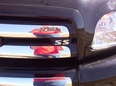 1988 Ford Bronco - Close-up of a chrome grille an "SS" badge, reflecting the photographer and the sky.