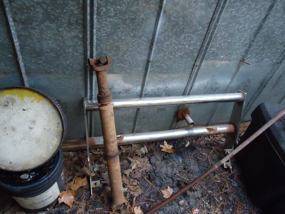 Rusty driveshaft and chrome bull bar leaning against a corrugated metal wall