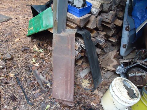 1985 Ford Bronco - A rusted metal panel lies on the ground next to a pile of firewood and other assorted parts.