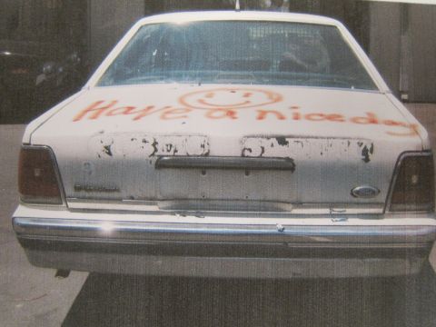 1991 Ford LTD Crown Victoria - printed photo shows the dented rear of a white Ford sedan with orange graffiti reading 'Have a nice day' and a smiley face.