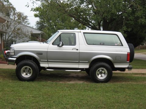 1994 Ford Bronco - Side profile of a two-tone 1994 Ford Bronco with aftermarket wheels and a spare tire mounted at the rear.