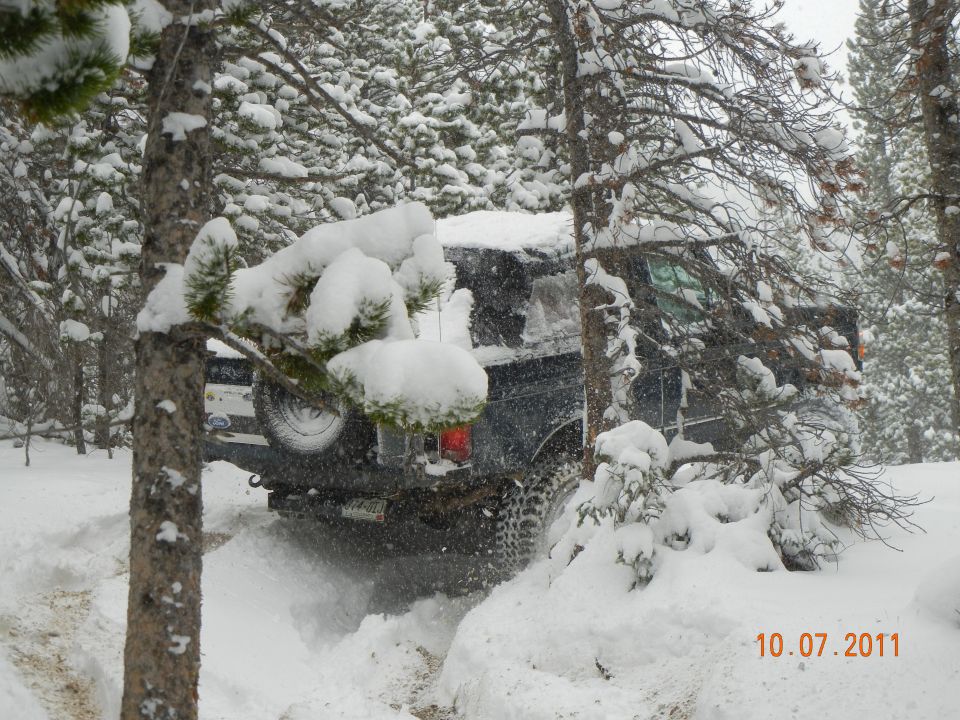Dark SUV driving through snow, spare tire visible on rear