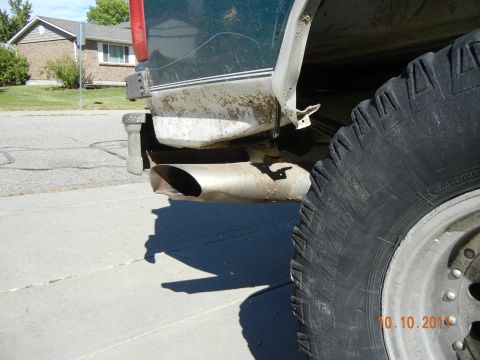 1996 Ford Bronco - A close-up view of a vehicle's rear tire and exhaust pipe, with a house in the background.