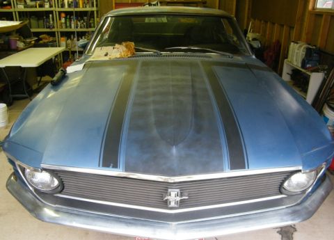 1970 Ford Mustang - The front end of a blue 1970 Ford Mustang is visible, black racing stripes on the hood and a chrome grille.