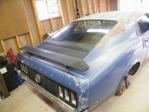 1970 Ford Mustang - Rear view of a 1970 Ford Mustang in a garage, showing peeling paint and a spoiler.