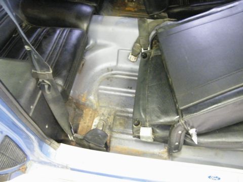 1970 Ford Mustang - Interior view of a blue car's floor, showing black seats and evidence of rust on the metal floor pan.