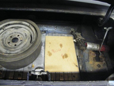 1970 Ford Mustang - The trunk of a vehicle contains a spare tire, jack, and a piece of cardboard with writing on it.