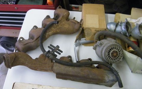 1970 Ford Mustang - Exhaust manifolds and alternator parts are laid out on a table, possibly for repair or sale.