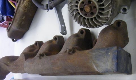 1970 Ford Mustang - Close-up of an old exhaust manifold and a fan shroud, showing signs of rust and wear.