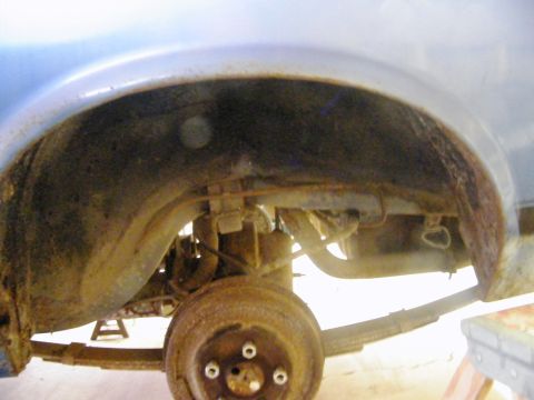 1970 Ford Mustang - The rear wheel well and suspension components are visible, with significant rust present on the drum brake and surrounding metal.