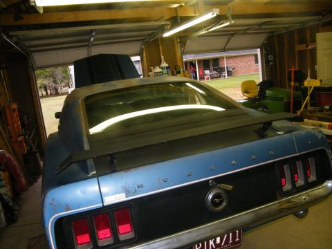 1970 Ford Mustang - Rear view of a blue 1969 Ford Mustang with a black spoiler and taillight panel, parked inside a garage.