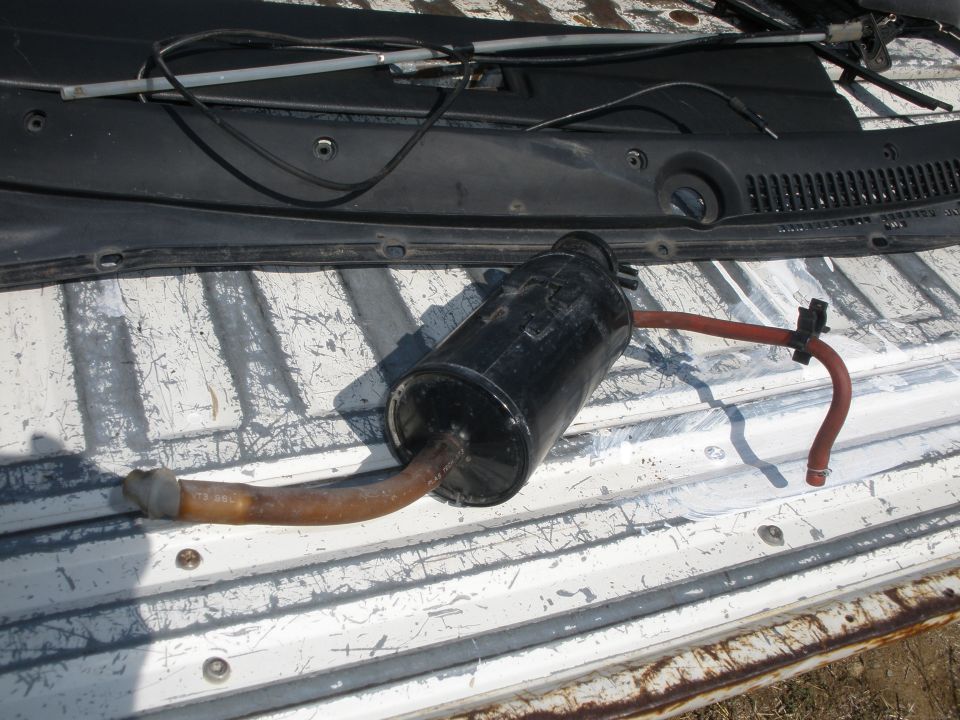 Exhaust muffler with bent pipe and red hose attached, lying on a white ribbed surface