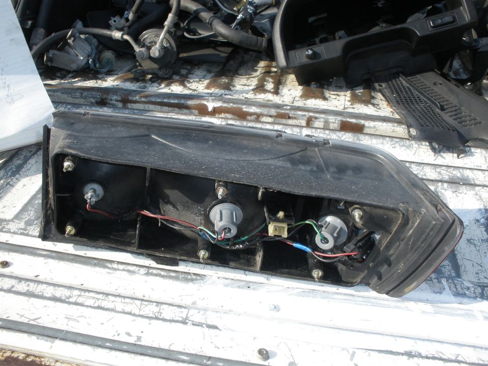 Black taillight assembly with exposed bulbs and wiring, resting on a white truck bed