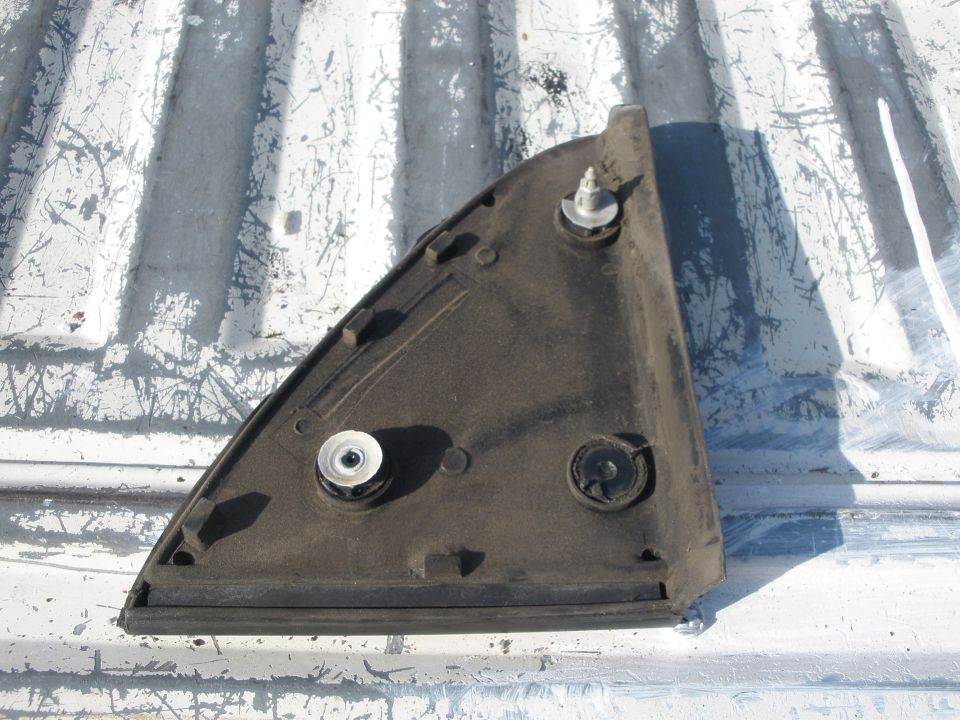 Black plastic car mirror trim piece with two mounting screws, lying on a white ribbed surface