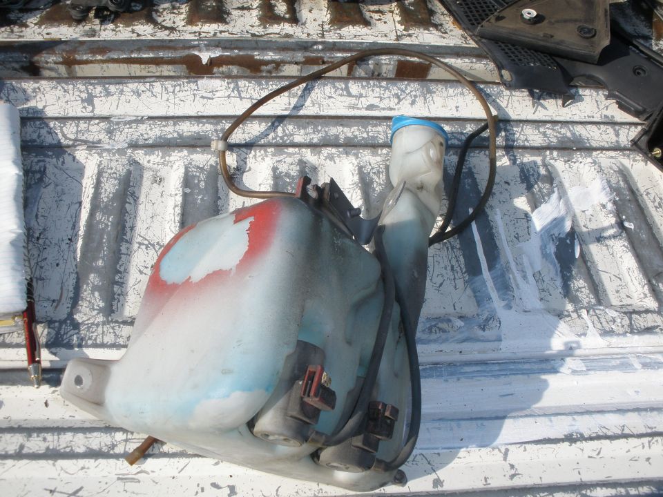 windshield washer fluid reservoir with hoses and blue cap, sitting in truck bed