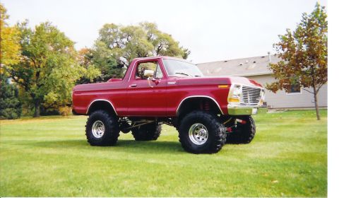 1978 Ford Bronco - A red 1978 Ford Bronco with a two-tone red-over-tan hood, lifted on a tall suspension with oversized mud tires and chrome wheels, parked on…
