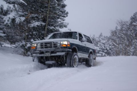 1996 Ford Bronco - A two-tone Ford Bronco navigates a snowy, wooded area during a snowfall.