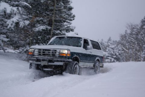 1996 Ford Bronco - A Ford Bronco navigates a snowy road with trees in the background.