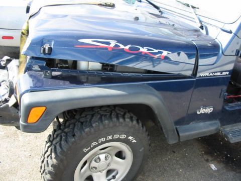 2002 Jeep Wrangler - The front end of a blue 2002 Jeep Wrangler shows significant damage, with the hood crumpled and torn.