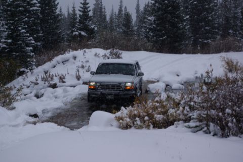 1996 Ford Bronco - A silver Ford Explorer navigates a snowy, watery path in a wooded area.