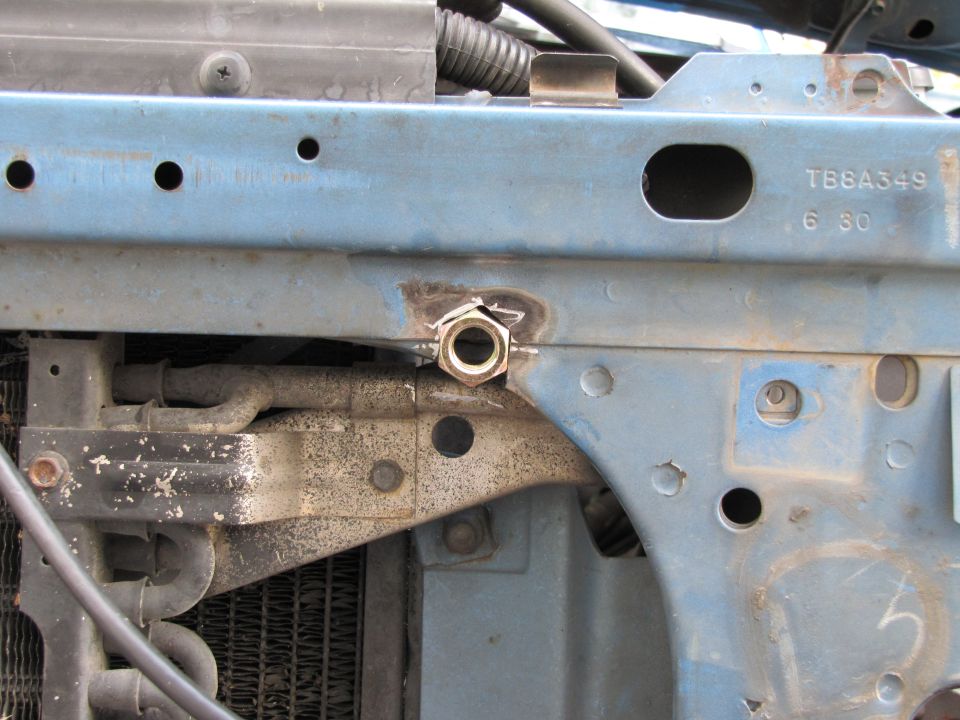 Close-up of blue painted metal brackets and hoses in a vehicle's engine bay, with a nut welded to one bracket