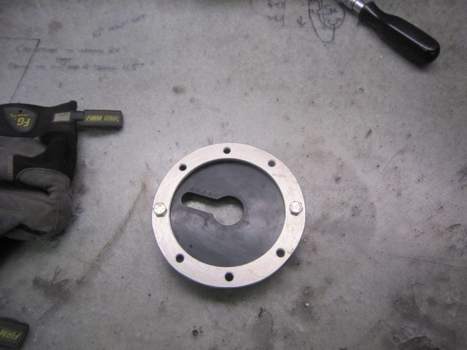 Metal and rubber fuel filler cap with bolt holes and a keyhole-shaped opening