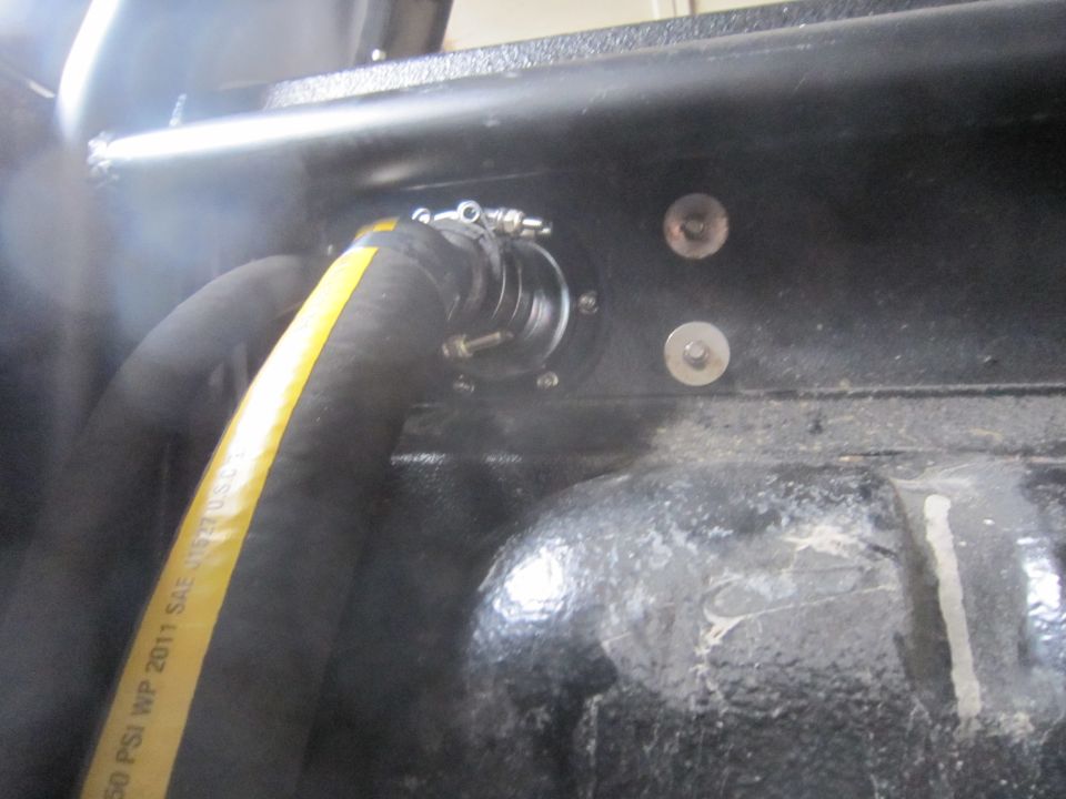 Close-up of a fuel filler neck with a yellow-striped hose attached, mounted in a black textured surface