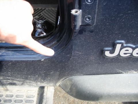 2002 Jeep Wrangler - A finger points to the door seal of a dark blue Jeep Wrangler, revealing scuff marks on the frame.