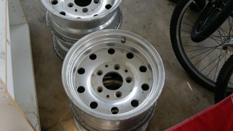1978 Ford Bronco - Several aluminum wheels are stacked on a concrete floor next to a bicycle wheel.