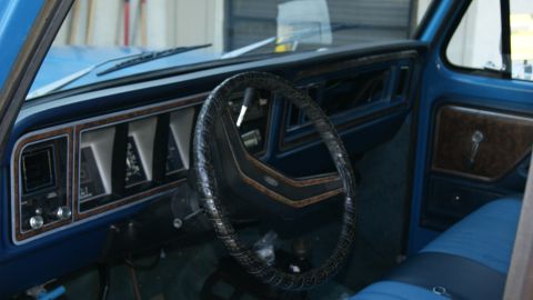 1978 Ford Bronco - Interior view of a blue truck, a patterned steering wheel and woodgrain dashboard accents.
