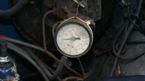1978 Ford Bronco - A close-up view of an old, weathered engine gauge with visible rust and wiring in the background.