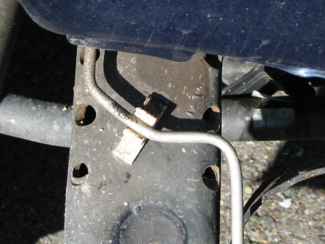 Close-up under a dark blue vehicle showing a black frame bracket with a metal brake or fuel line routed across it