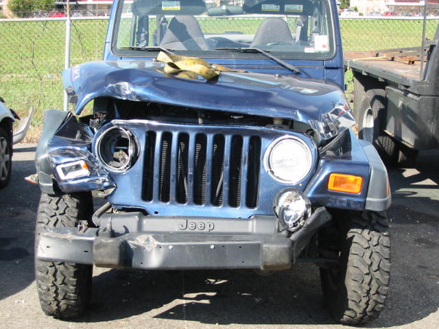 Front-end collision damage on a blue Jeep Wrangler with missing headlight