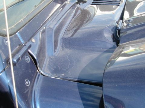 2002 Jeep Wrangler - Close-up view of the hood hinge and cowl panel on a dark blue vehicle.