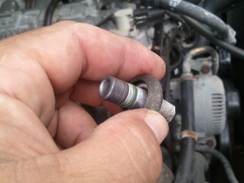 1994 Ford Bronco - Close-up of an AC Schrader valve being held, with engine parts visible in the blurred background.