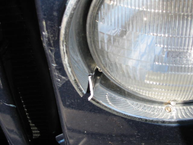 Cracked round headlight bezel and scuffed dark blue body panel after a collision