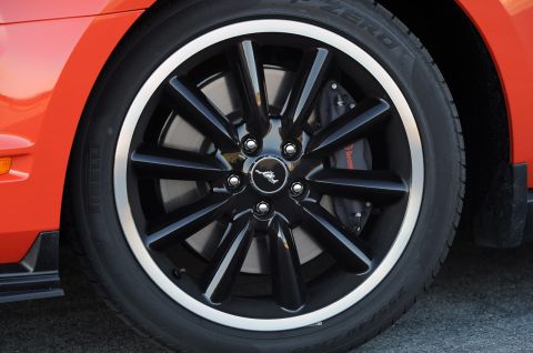 1993 Ford Taurus - Close-up of a black multi-spoke wheel with silver trim and a running horse emblem, part of an orange vehicle.