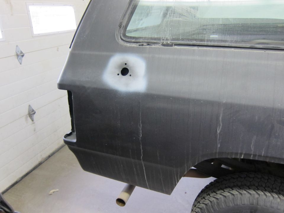 Rear quarter panel of a dark vehicle with a primer spot and three holes